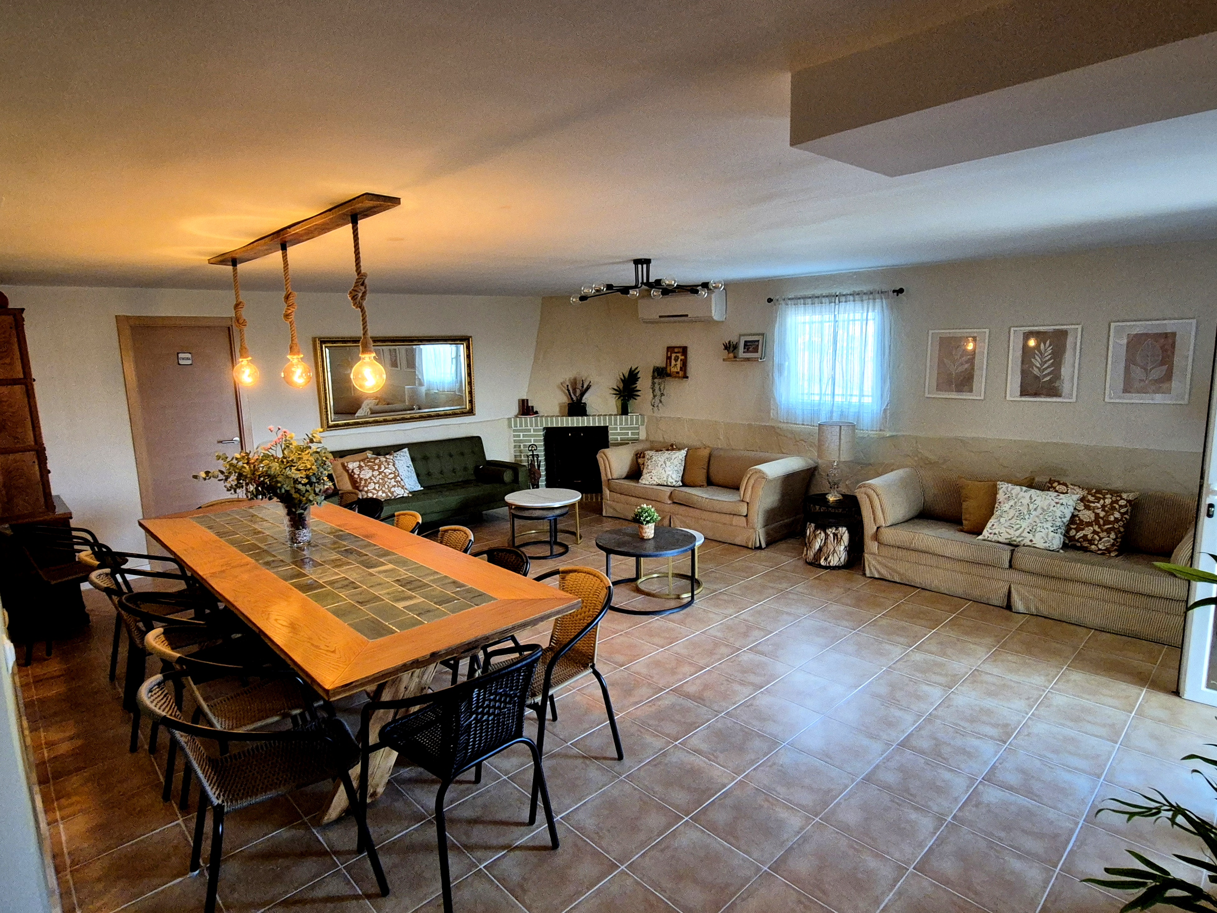 [Image description: A brightly lit living room with a dining area and two sofa beds, featuring a prominent light fixture c...